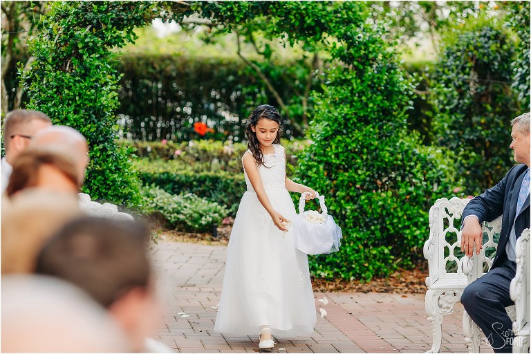 flower girl throws rose petals as she walks down aisle at Town Manor wedding ceremony