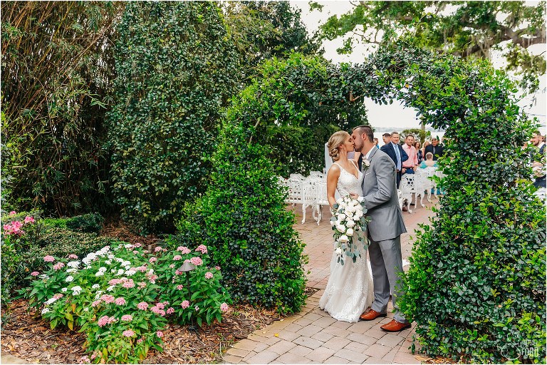bride & groom kiss under heart archway as loved ones clap at Town Manor wedding ceremony