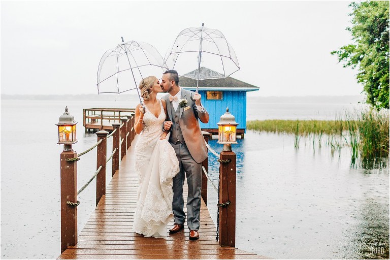 bride & groom kiss under umbrellas as the rain comes down around them at their Town Manor wedding