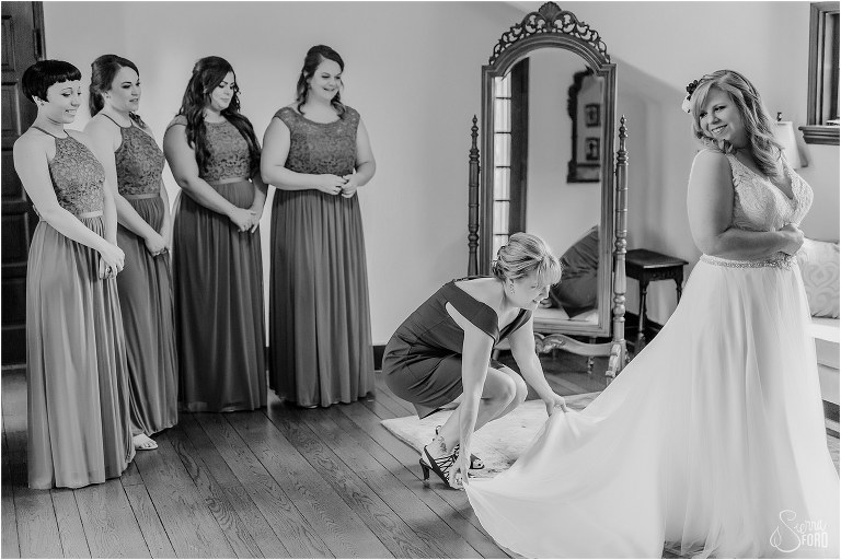 mother of the bride fluffs bride's dress as bridesmaids look on before Winter Park wedding