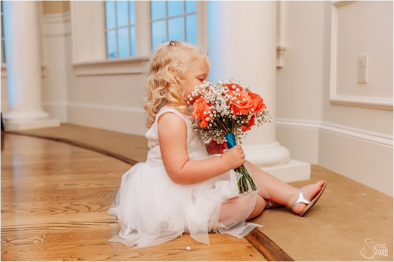 flower girl sits on the floor considering the bridal bouquet for a snack at River House wedding reception