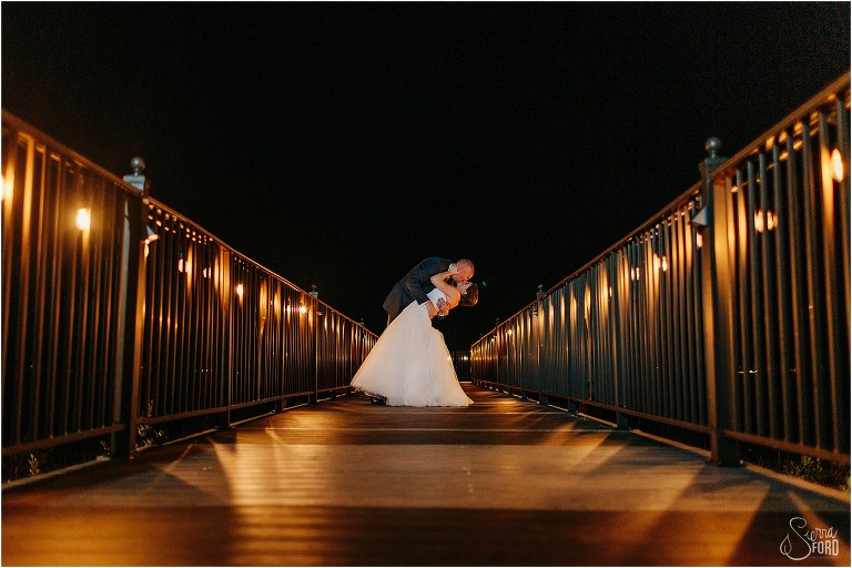 groom dips bride in a kiss as twinkle lights light up the dock at their River House wedding