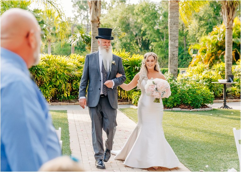 bride is beaming as father walks her down the aisle for Disney themed garden wedding ceremony
