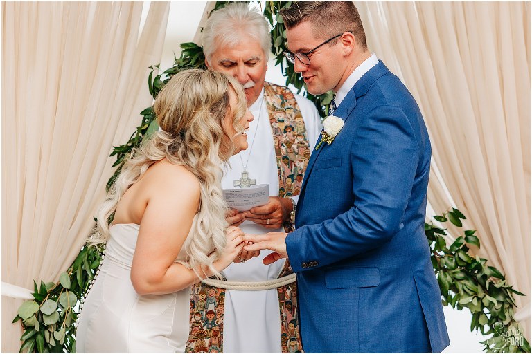 bride & groom laugh as bride tries to place wedding ring on groom's finger during Disney themed garden wedding ceremony