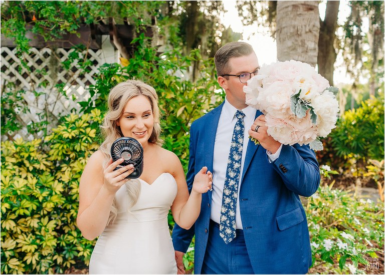 groom smells bridal bouquet while bride uses handheld fan at scorching Disney themed garden wedding