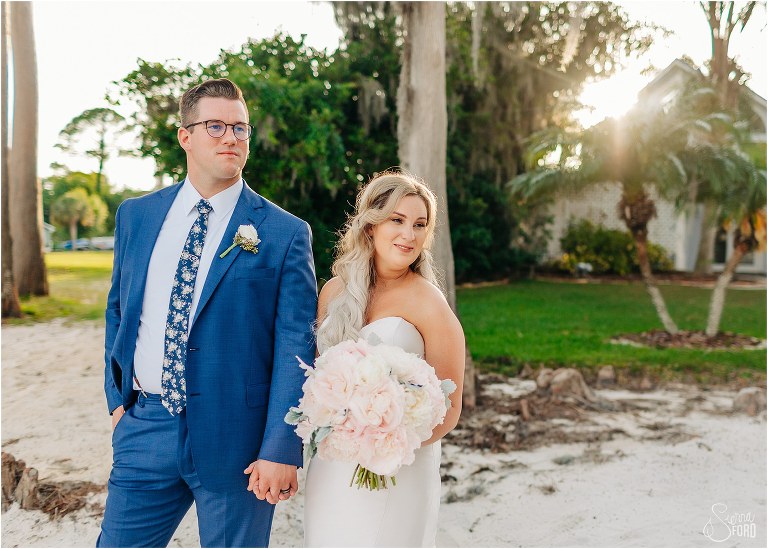 bride & groom walk hand in hand down beach as sun sets at Disney themed garden wedding