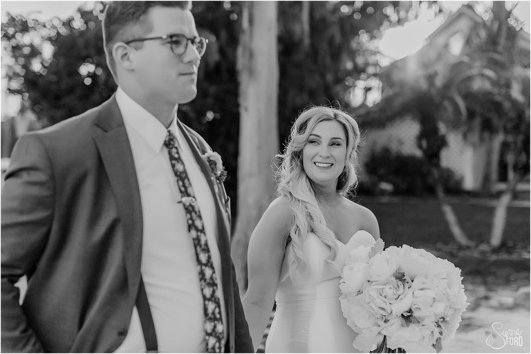 bride sneaks a peek at groom as they walk down the beach at Disney themed garden wedding