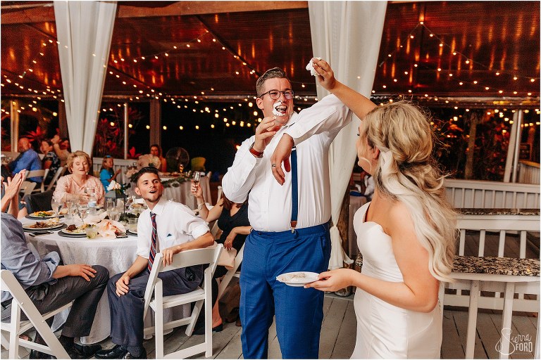 groom tries to block bride from smashing cake in his face at Disney themed garden wedding reception