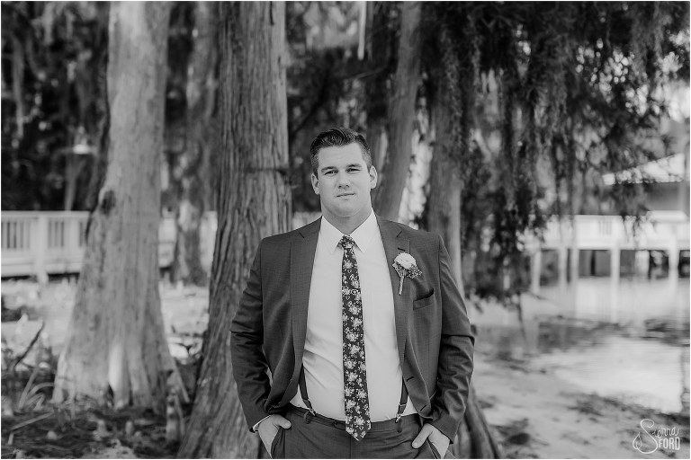 groom stands among trees on the sand before Disney themed garden wedding