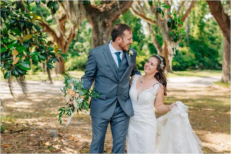 bride & groom laugh as he carries her bouquet through the trees at Savannah elopement