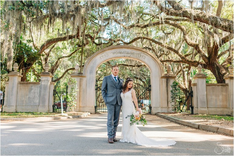 bride & groom pose in front of old Wormsloe Plantation gate under oak trees at Savannah elopement