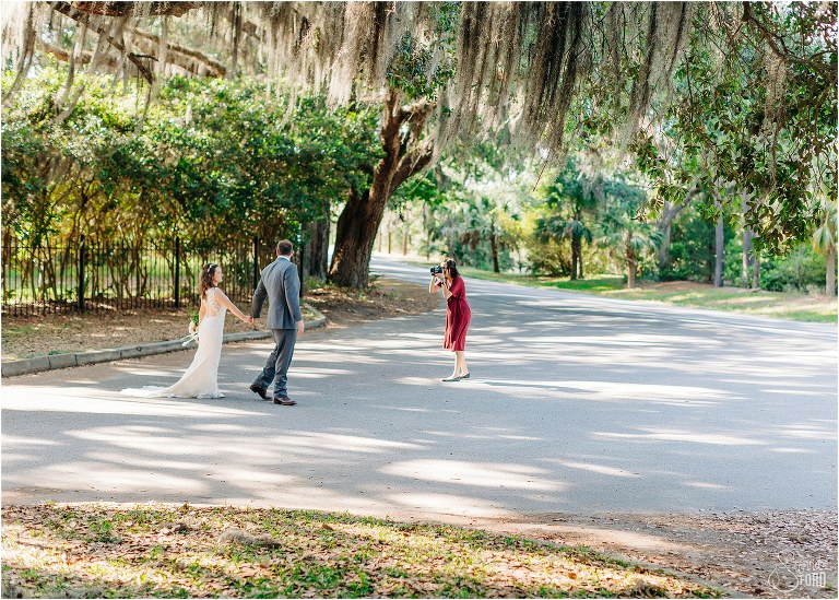 behind the scenes shot of Sierra Ford Photography capturing bride & groom walking through Wormsloe Plantation at Savannah elopement