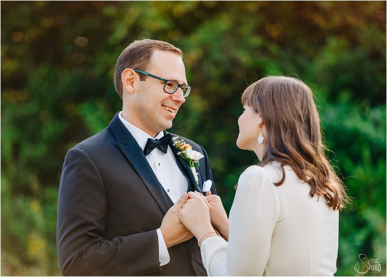 groom smiles lovingly down at bride before elegant backyard elopement