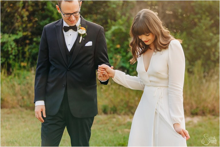 groom guides bride as they walk together before elegant backyard elopement