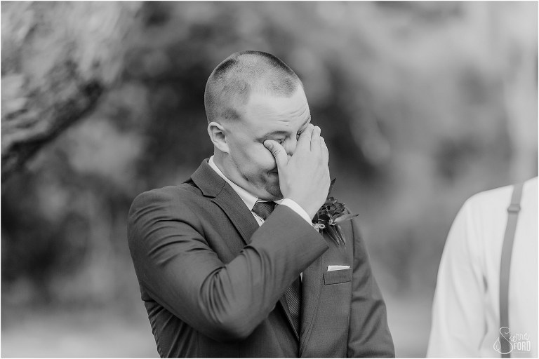groom wipes away tears as he sees his bride coming down aisle at DIY Florida Barn Wedding