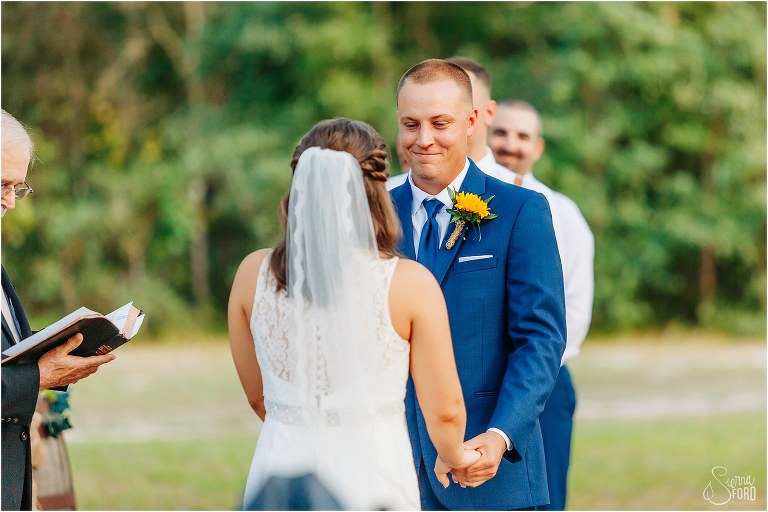 emotional groom smiles at bride as he recites his vows at DIY Florida Barn Wedding