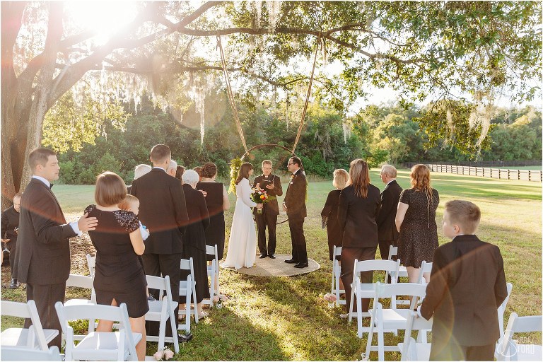sun shines through live oak tree as bride & groom exchange vows at elegant florida elopement ceremony