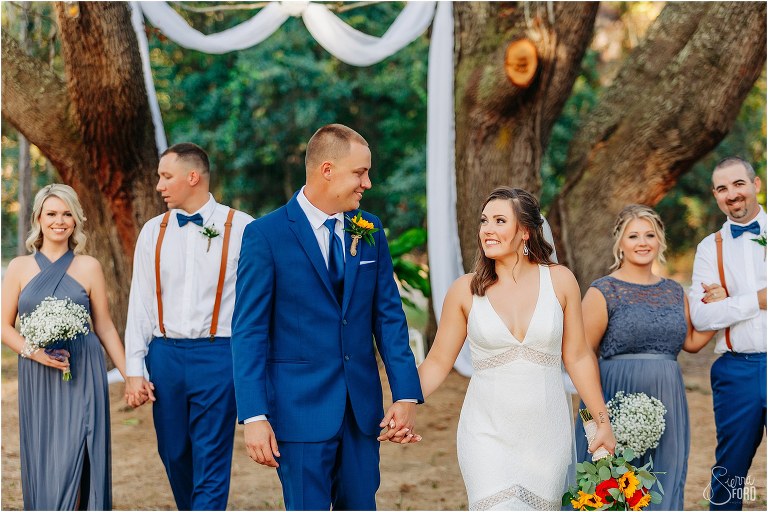 bride & groom smile at each other as they walk with wedding party at DIY Florida Barn Wedding