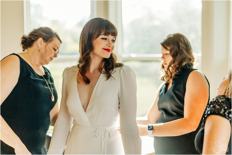 bride's mother and bridemaids finish zipping bride's Reformation dress before elegant backyard elopement