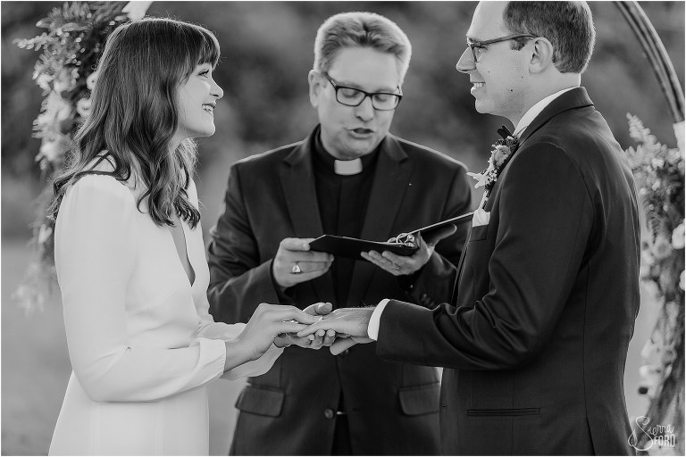 bride places ring on groom's finger during elegant backyard elopement ceremony