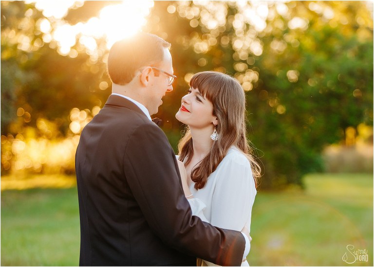 bride looks lovingly up at groom as he talks to her while sun sets behind them at elegant backyard elopement
