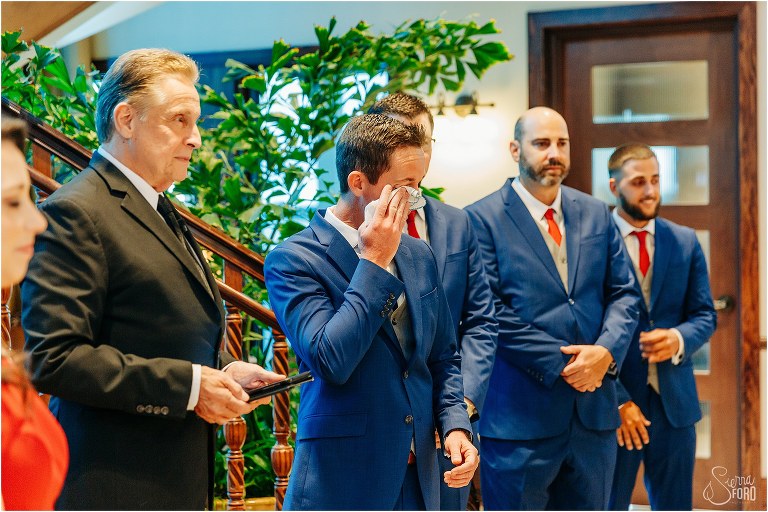 groom wipes away tears as he sees bride come down aisle at waterfront wedding ceremony