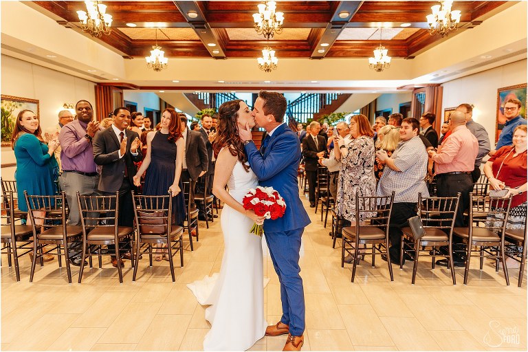 bride & groom kiss as loved ones cheer at end of waterfront wedding ceremony