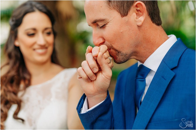 groom kisses his new wife's hand at waterfront wedding