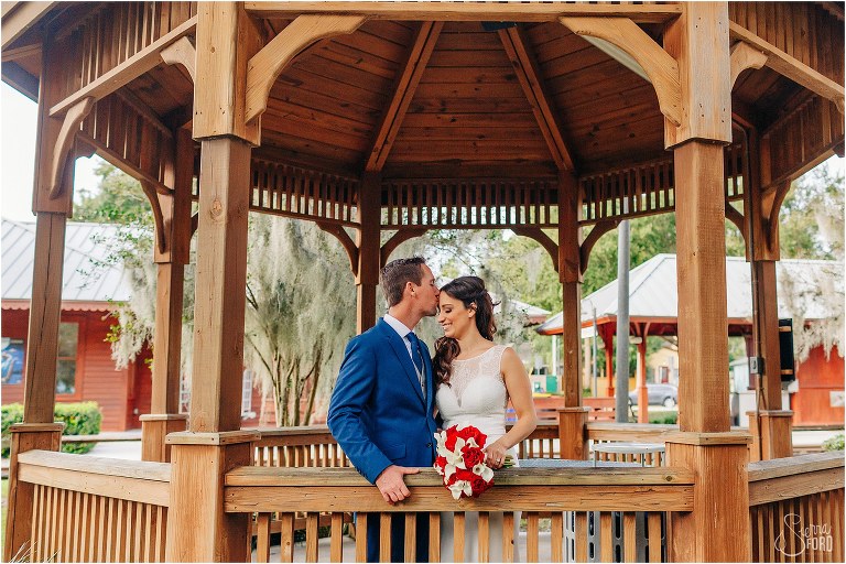 groom kisses bride's forehead in pavilion in Wooten Park at waterfront wedding
