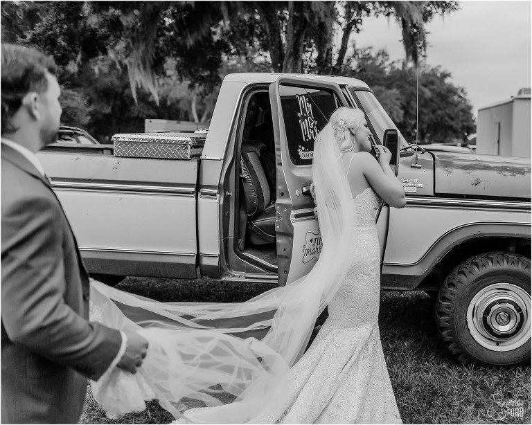 groom holds bride's train as bride reapplies lipstick at Horsepower Ranch wedding