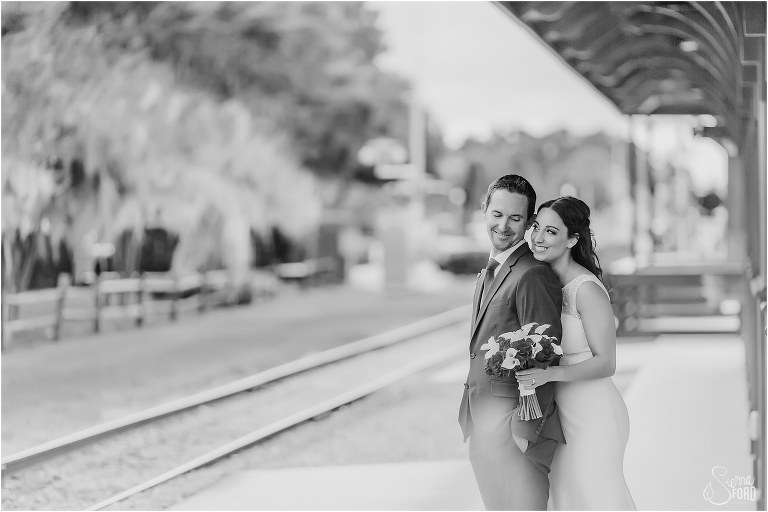 bride comes up behind groom at Tavares train station during waterfront wedding