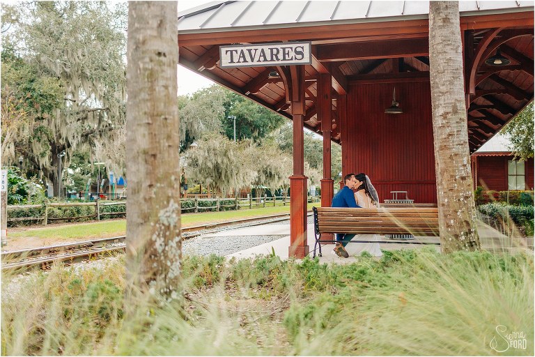 bride & groom cuddle up on bench at Tavares train station at waterfront wedding