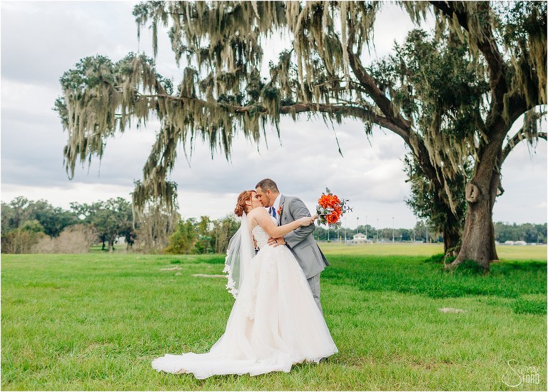 groom kisses bride passionately under oak tree at Wildwood wedding