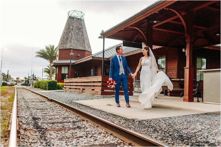 bride & groom walk hand in hand by train tracks at waterfront wedding