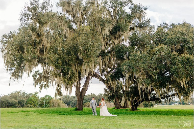 groom leads bride under huge oak tree with Spanish moss at Wildwood wedding