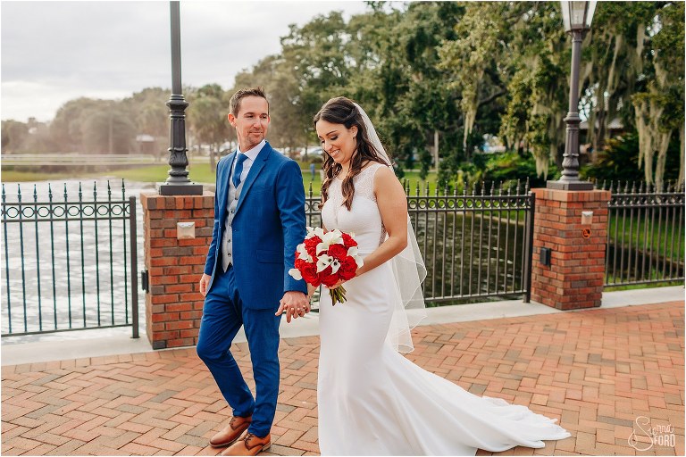 groom stares lovingly at bride as they walk down pier at waterfront wedding