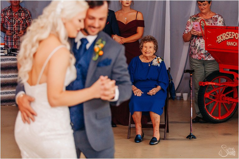 bride's grandmother smiles lovingly as she watches bride & groom dance together at Horsepower Ranch wedding