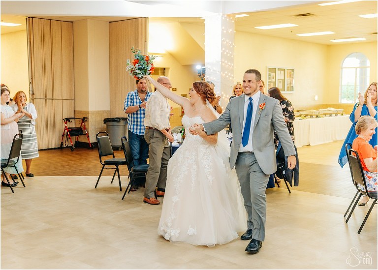 bride raises bouquet triumphantly as the couple enters their Wildwood wedding reception