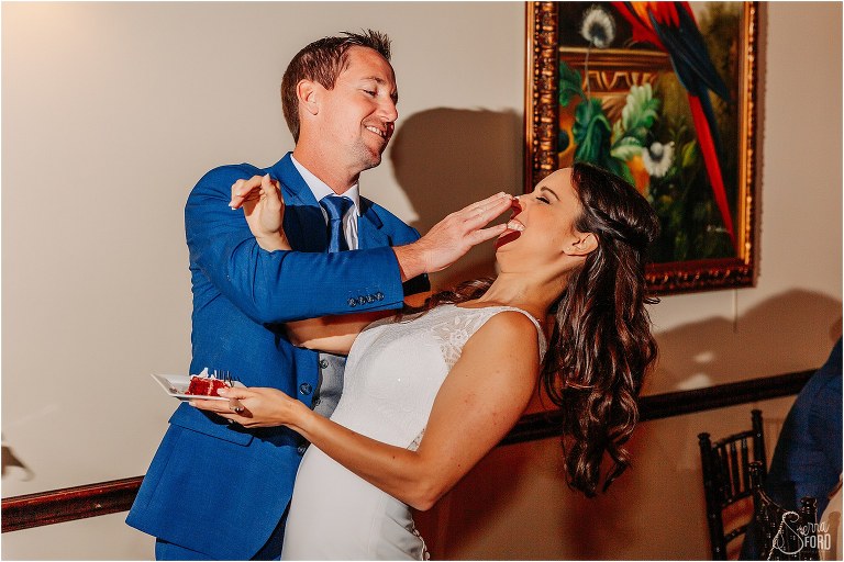 groom playfully shoves cake onto bride's nose at waterfront wedding reception