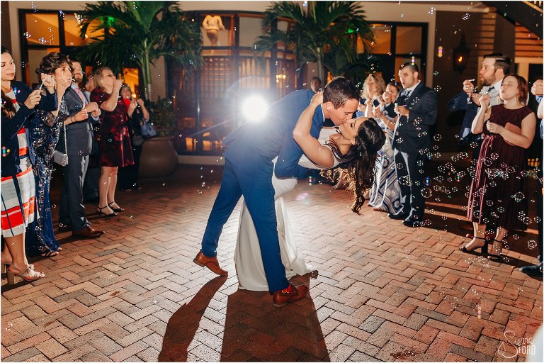 groom dips bride dramatically and kisses her during bubble exit from waterfront wedding reception