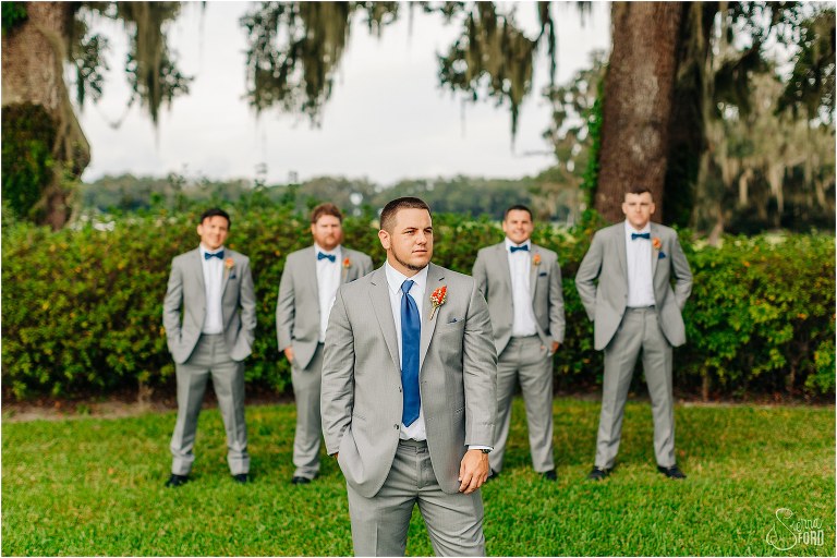 groom stands under oak tree with groomsmen in slate grey Men's Wearhouse suits before Wildwood wedding