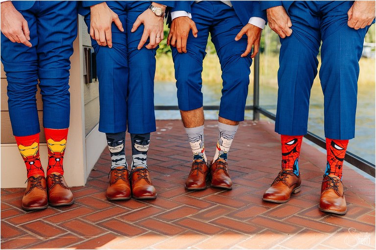 groom and groomsmen show off superhero socks before waterfront wedding