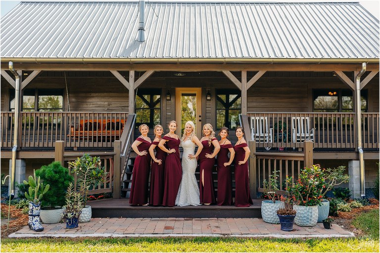 bride poses with bridesmaids in front of bride's cabin before Horsepower Ranch wedding