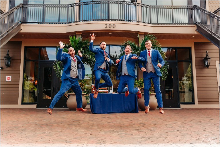 groom & groomsmen jump with joy before waterfront wedding