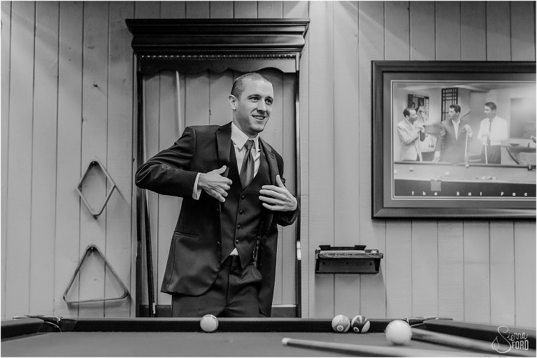 groom puts suit jacket on in billiard room as he prepares for Mission Inn Resort wedding