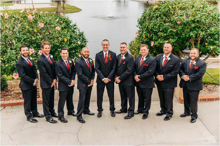 groom laughs with groomsmen in black suits with red accessories at Mission Inn Resort wedding