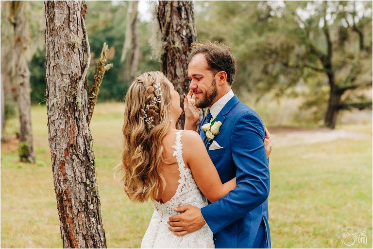 bride wipes tears from groom's eye during first look at lakefront wedding