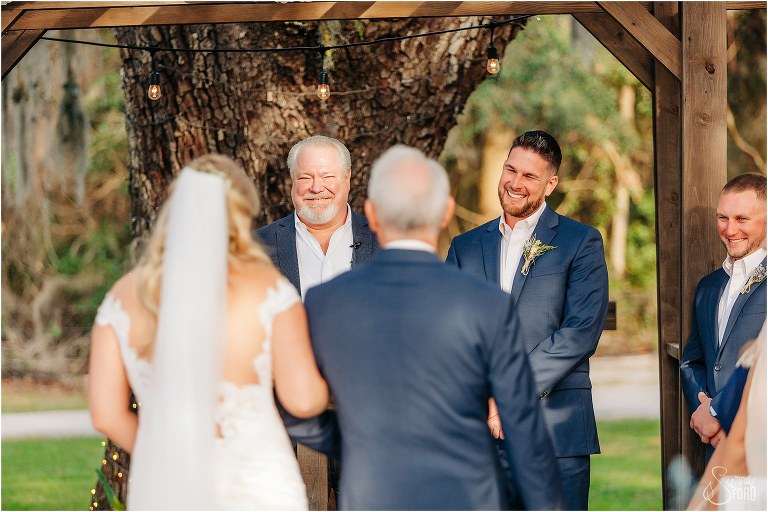 groom smiles from ear to ear as bride comes down aisle at Ever After Farms wedding