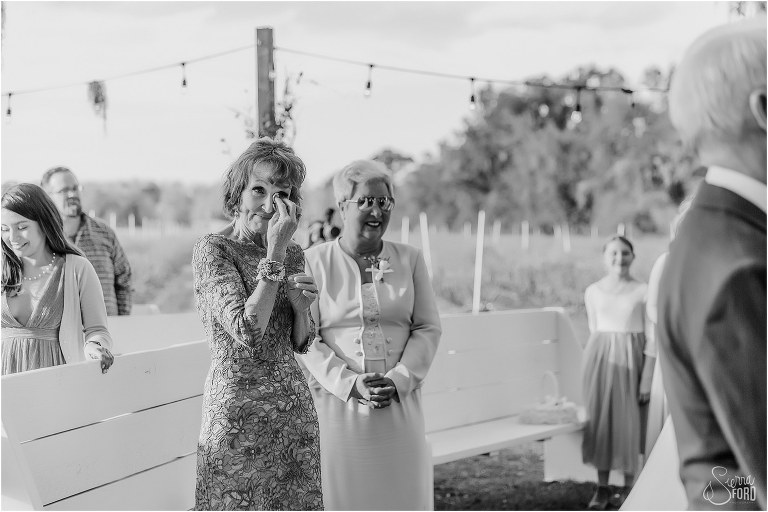 mother of the bride wipes tears from her eyes as daughter comes down aisle at Ever After Farms wedding