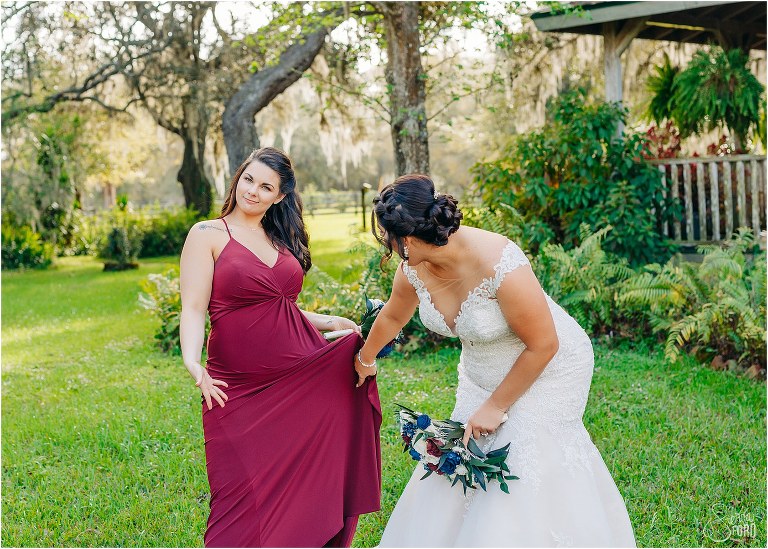 bride laughs as bridesmaid shows off dress at Isola Farms wedding